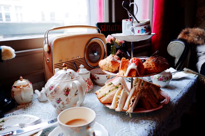 An Afternoon Tea stand with sandwiches, cakes, and jams and cream, alongside a vintage radio and teapot