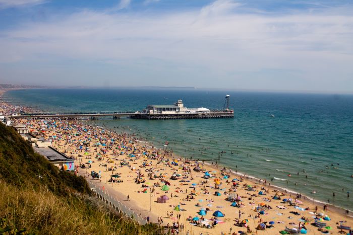 Bournemouth beach from a distance, showing a busy beach full of tourists, a blue sea, and the pier.