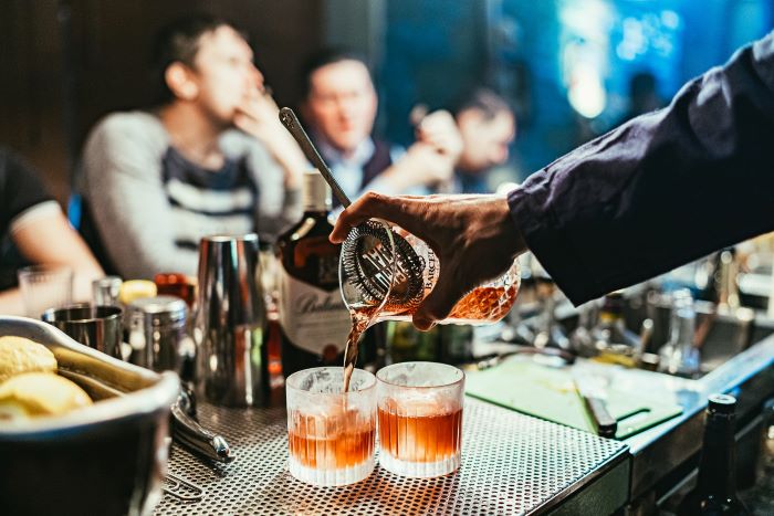 Alt: A hand holding a cocktail glass and strainer pours two cocktails into frosted glasses on a cocktail bar.