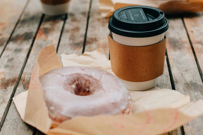 a takeaway coffee and a glazed doughnut on a table