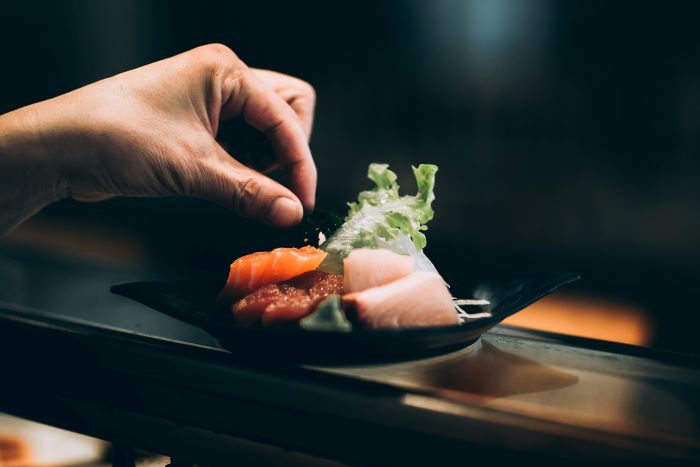 A hand sprinkling some salt on a small plate of sushi