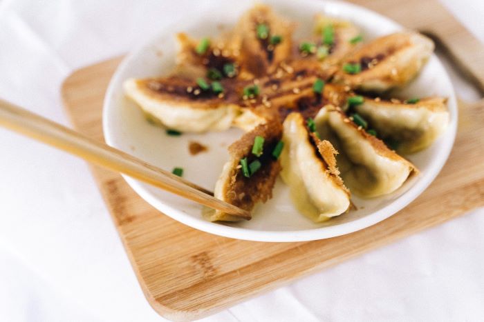 A pair of chopsticks taking a piece of crispy gyoza from a plate.