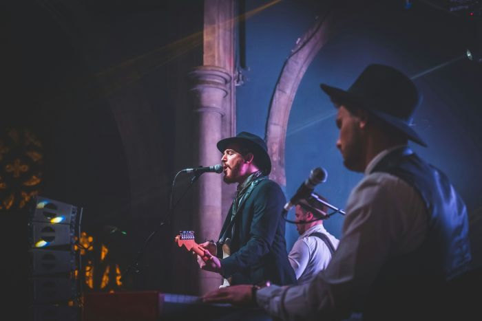 A three-piece band on stage with a musician singing into a microphone