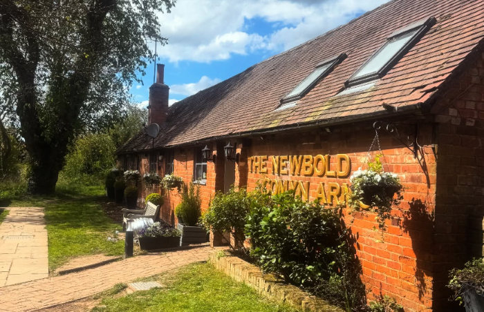The exterior of the Newbold Comyn Arms with a bench, trees, and hanging baskets.