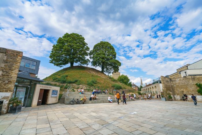 Oxford Castle Mound with two trees on top and people exploring the Castle Quarter.