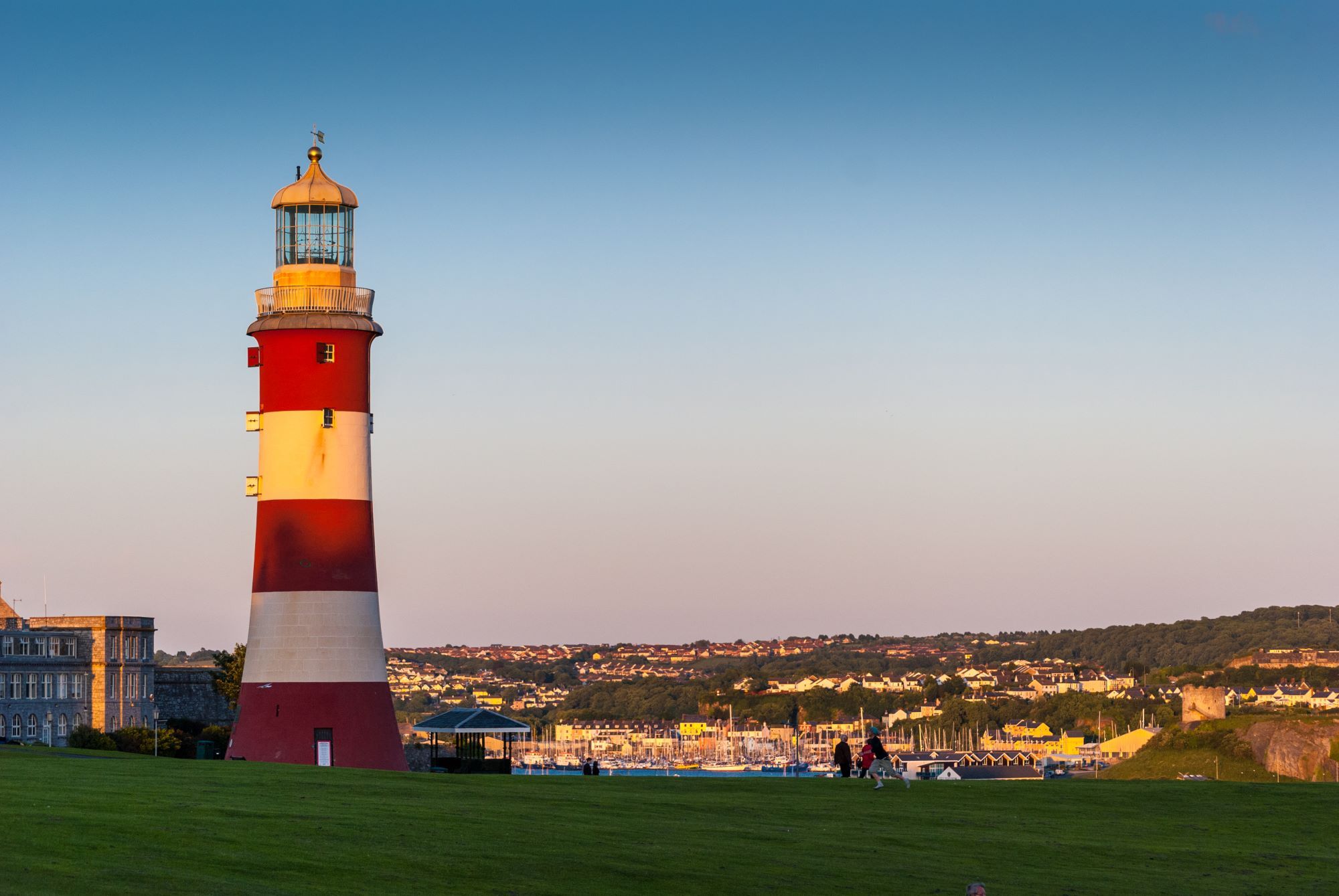 View of Plymouth Hoe at dusk, with a cloudless sky overlooking the lighthouse and harbour below.