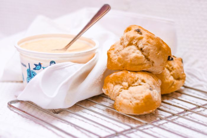 A pot of clotted cream with a spoon in, alongside a small pile of fruit scones
