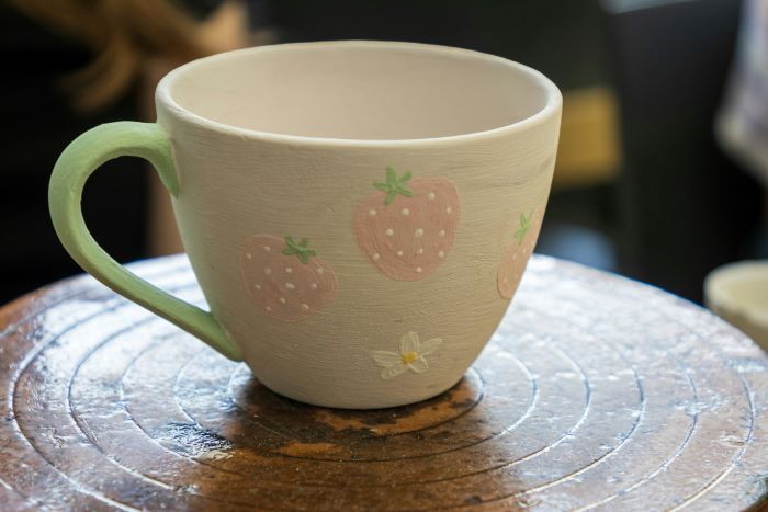 An unglazed tea cup with strawberries and white flowers on it.