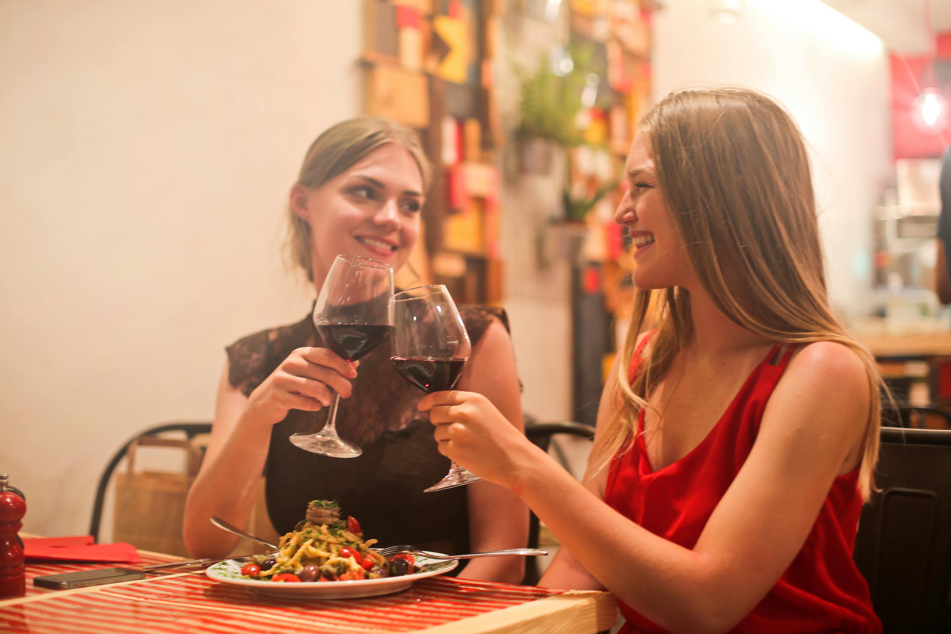 Two women touching wine glasses at dinner